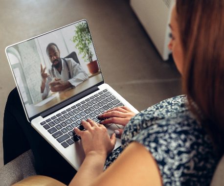 Woman sitting in front of laptop watching a video of a male doctor speak to camera